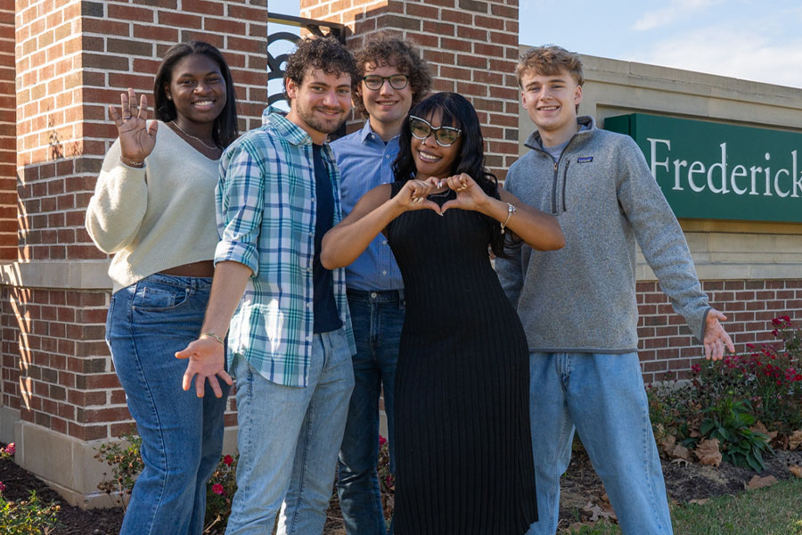 group of students in front of fcc sign make heart sign with hands
